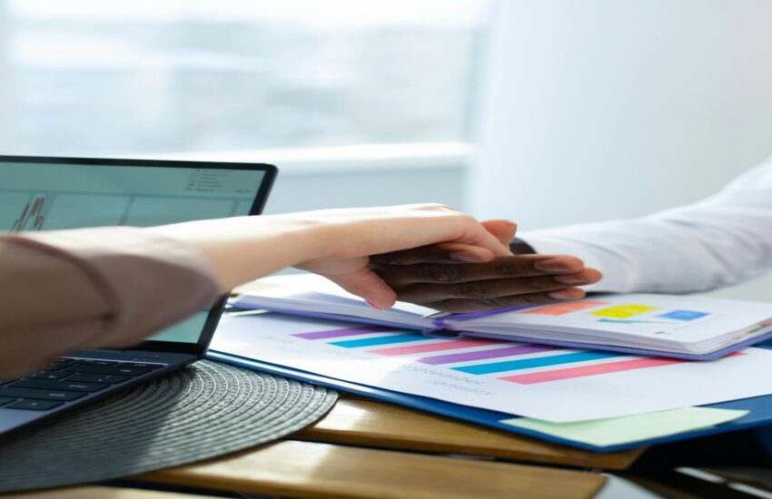 Business handshake between two professionals discussing student loan refinancing options, with financial charts and documents on the table